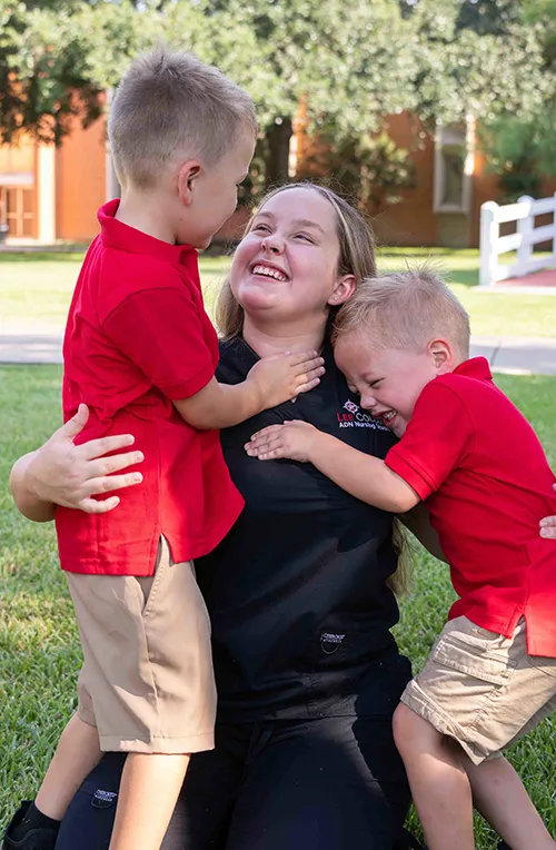 Two young boys hug a woman outdoors.