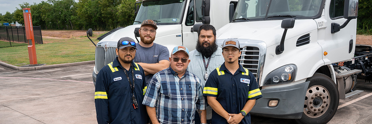 Five men pose before tractor-trailer rigs in a parking lot.