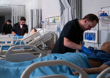 Students work on practice dummies in hospital beds