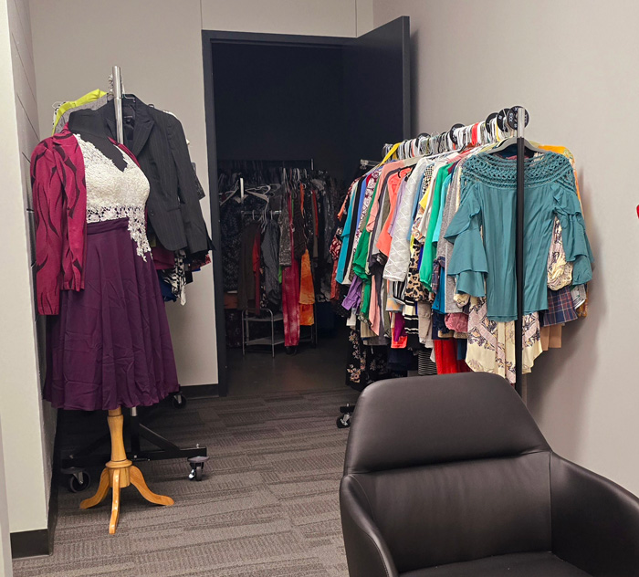 A photograph of the Clothing Closet inside the Student Resource and Advocacy Center. On the left, a mannequin is shown wearing a purple knee-length dress, decorated with white lace. To the right, a rack displays a selection of clothing items available.