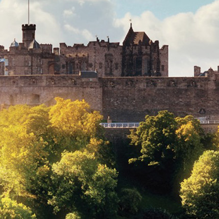 A castle on rocky terrain with trees in the foreground.